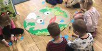 Dzieci przyklejają niebieskie karteczki do plakatu przedstawiającego Ziemię.