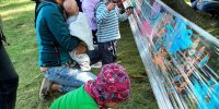Dzieci i rodzice malują farbami po foli owiniętej wokół drzew