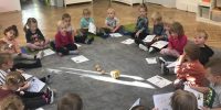 Dzieci siedzą na dywanie, a na środku są postawione różne dynine