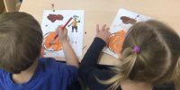 Dziewczynka i chłopiec malują farbami ilustrację dynie
