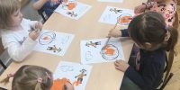 Dzieci przy stoliku malują farbami ilustrację dyni