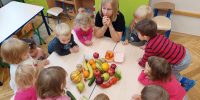 Dzieci i Pani zgromadzone wokół stolika, na środku leża różne owoce i warzywa