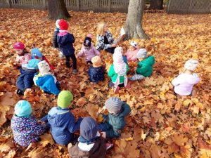 Nauczyciel czyta książkę dzieciom. Wszyscy siedzą na jesiennych liściach w ogrodzie przedszkolnym