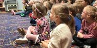 Dzieci siedzące na dywanie, wpatrują się w przedstawienie