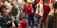 Dzieci wraz z pomocnikiem Świętego Mikołaja tańczą na dywanie