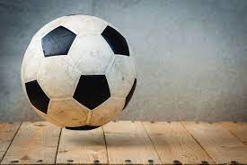 piłka do gry w piłkę nożną - czarno- biała uniesiona nad drewnianą podłogą